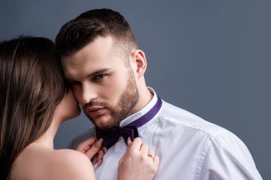 Kadın, erkeğin papyonunu, papyonunu tutuyor. Aşık seksi bir çift. Şehvetli aşıklar soyunur. Kız arkadaş ve erkek arkadaş şehvetli kucaklaşmalar. Erkek kıza romantik kucaklaşma. Şefkatle sarıl. Çıplak tutku vücudu.