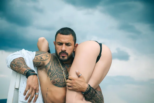 Man holding woman with sexy hot ass. Strong muscular tattooed bearded man holding his sexy fit woman with hot butt isolated at grey background. Eternal love and trust concept. —  Fotos de Stock