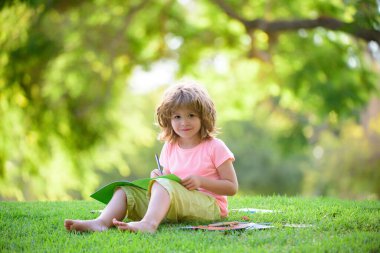 Parkta okuyan sevimli küçük bir öğrenci ve açık havada çocukların eğitimi için gülümsüyor.
