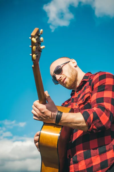 Man with guitar on sky. Handsome boy wearing sunglasses and playing guitar. — Stock Photo, Image