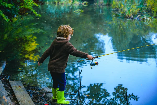 Criança bonito menino puxando haste enquanto a pesca no lago. — Fotografia de Stock