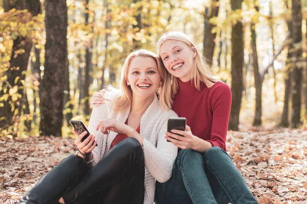 Usmívající se mladé ženy s mobilem v podzimním parku. Přátelství dívky koncept, usmívající se přítelkyně s chytrými telefony. — Stock fotografie