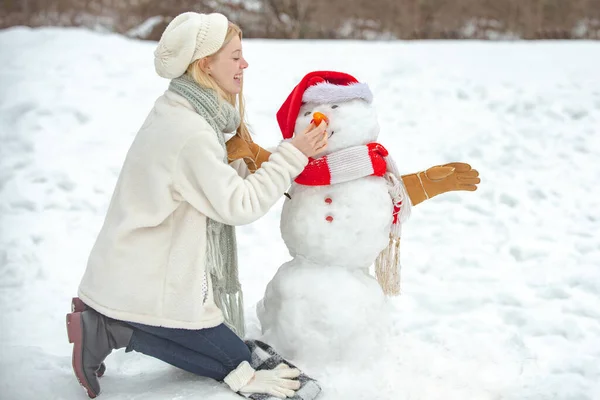 Muñeco de nieve y modelo femenino divertido de pie en sombrero de invierno y bufanda con nariz roja. Feliz invierno. Sensual chica de invierno posando y divirtiéndose. — Foto de Stock