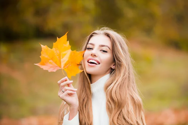 秋を背景に黄色いカエデの葉を手にした幸せな笑顔の女性。秋の日には可愛い女の子がポーズをとって天気の良い日を楽しむ. — ストック写真