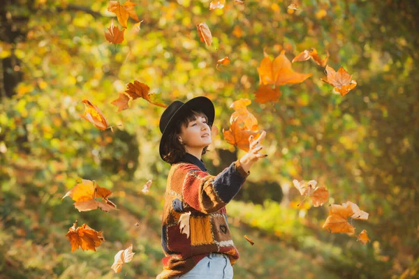 Pozytywna modelka odpoczywa. Jesienne liście spadają na szczęśliwą młodą kobietę w lesie. Koncepcja upadku. Jesienna kobieta w jesiennym parku. Piękna młoda kobieta rzucająca liśćmi w parku. — Zdjęcie stockowe
