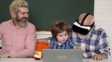 3 boyutlu VR gözlüklü büyükbaba. Mutlu olgun öğretmenler. Baba, büyükbaba ve oğul evde çalışıyor ve ev ödevi yapıyor. Çocuklar okula hazırlanıyor. Okulda tahtaya yakın bir çocuk..
