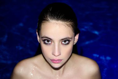 Havuzdaki bir kızın yakın çekim seksi portresi. Suyun mavi arka planında poz veren kadın.