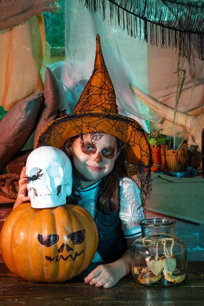 Hij lacht op een Halloweenfeest. meisje kind draagt Halloween kostuum met pompoen een oud houten huis. Fijne Halloween. Witch kind met truc of traktatie. — Stockfoto