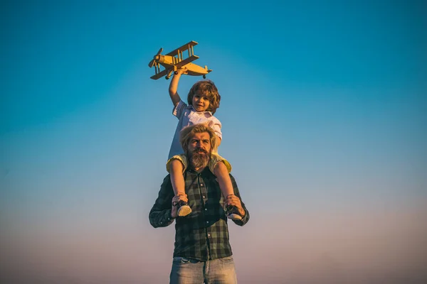 Father and son playing with wooden airplane. Father carrying his son on shoulders.