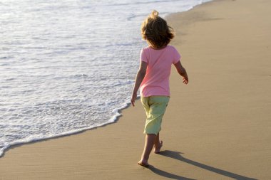 Aktif çocuk yaz tatilinde eğleniyor. Çocuk kumsalda koşuyor..