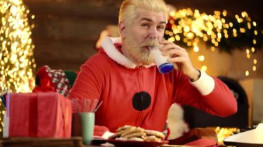Komik, modern Noel Baba evde Noel ağacının yanında süt içer. Yeni Yıl Tatili.
