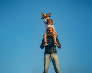 Baba oğlunu omuzlarında taşıyor. Baba oğul dışarıda oyuncak uçakla oynuyorlar. Aile tatili, ebeveynlik. Babalar Günü.