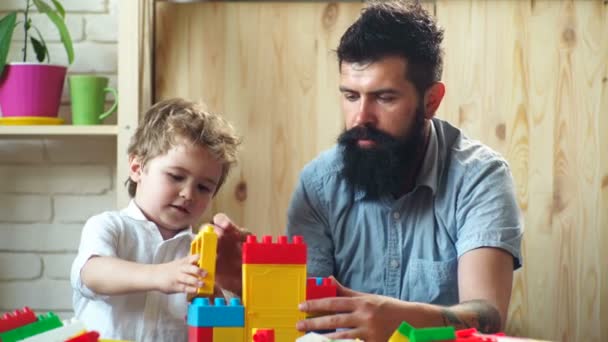 Jongen en bebaarde man spelen samen. Familie en kindertijd concept. Vader en zoon maken kleurrijke constructies met speelgoedstenen. Papa en kind bouwen huis van plastic blokken. — Stockvideo