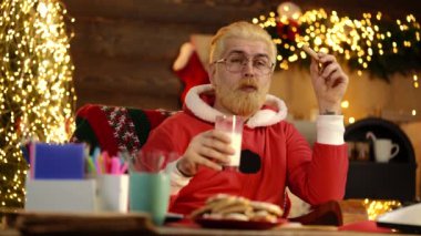 Komik Noel Baba evde masada kurabiye ve bir bardak süt topluyor.,