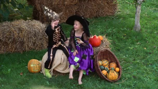 Glad bror och systrar på Halloween. Roliga ungar i karnevalsdräkter utomhus. Glada barn leker med pumpor hinkar på gården. — Stockvideo