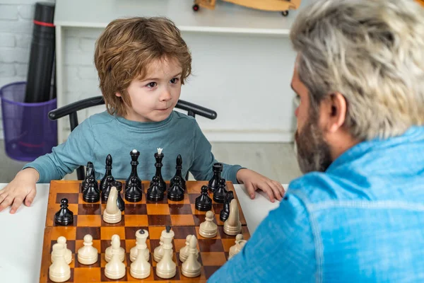 Inteligentní děti. Rodinná dovolená a sounáležitost. Roztomilý chlapec, který rozvíjí šachovou strategii. Muž učitel hrát šachy s předškolního dítěte. — Stock fotografie