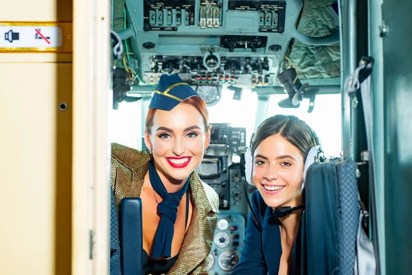 Beautiful woman pilot wearing uniform. Happy and successful flight. Looking at camera in plane. Girls looking at camera. Two Women Pilots Sitting in Cabin of Modern Aircraft.
