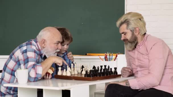 아버지와 아들은 집에서 할아버지와 체스를 두고 있습니다. 아이들은 일찍 발전 합니다. 식탁에 앉아 체스를 두고 있는 착하고 농축 된 소년. 체스, 성공과 승리. 음 가족. — 비디오