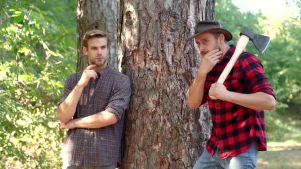 Zwei kräftige Männer Holzfäller mit Axt im karierten Hemd. Hübsche Holzfäller mit einer großen Axt untersuchen den Baum vor dem Fällen. Brennholz als erneuerbare Energiequelle. — Stockvideo