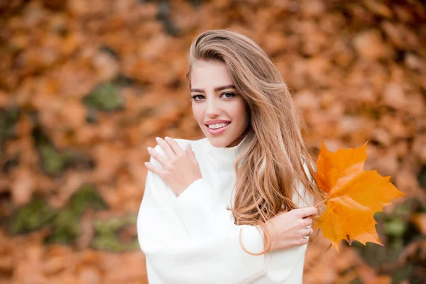 Felice donna sorridente che tiene in mano foglie d'acero gialle su sfondo autunnale. — Foto Stock