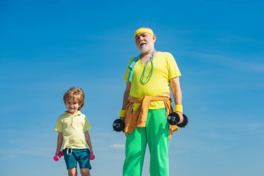 Büyükbabanı izle. Baba ve çocuk eğitimi. Büyükbaba ve çocuk sabah egzersizi yapıyorlar. Küçük çocuklar için spor. Dedesiyle küçük mutlu çocuk halterleriyle egzersiz yapıyor..