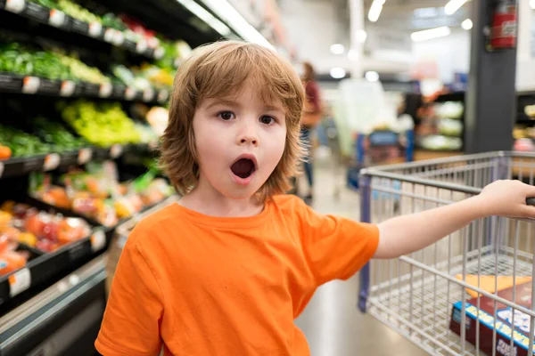 Compras engraçadas. Menino bonito alegre no supermercado compra verduras. Alimentos saudáveis para crianças. — Fotografia de Stock