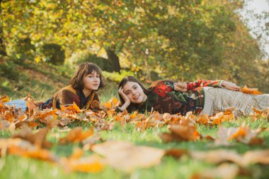 Parktaki çimenler tamamen sarı yapraklarla kaplı. Sonbahar Parkı 'nda Düşen Sonbahar Yaprakları ile Eğlenen İki Kadın Renkli Ağaçlar Arasında.