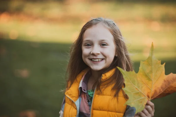 Giocare con le foglie. Adorabile ragazza felice con le foglie cadute in mano. Bambina in autunno con foglie d'arancio. Bella ragazza felice divertirsi nel parco autunnale. — Foto Stock