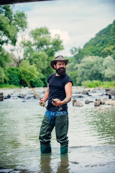 Un pescatore ha un pesce in mano. Felice gente allegra. Pesca nel fiume. Pescatore cattura il pesce. Un uomo barbuto che cattura pesci. Pescatore mostra tecnica di pesca uso canna. Divertiti.. — Foto Stock