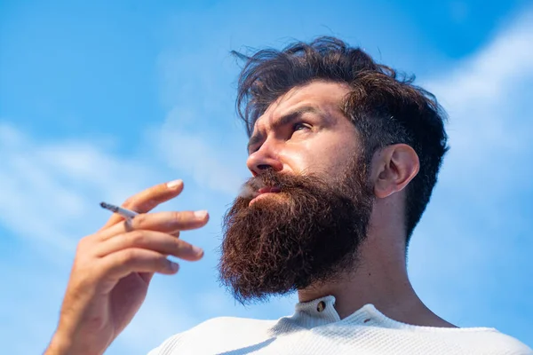 Bonito elegante jovem fumando fora, olhando para longe. — Fotografia de Stock