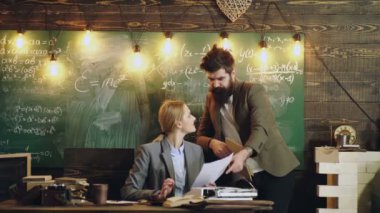 Profesör, genç bayana sınıfta tahtaya karşı kitap tutmasında yardım ediyor. Kadın asistan.