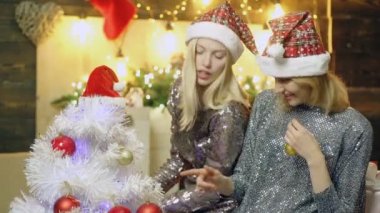 İki mutlu noel kızı. Noel Baba şapkalı tatlı bir kadın gülümsüyor, eğleniyor. Moda kadınları. Güzel Kız Kardeşler Arkadaşları. Modayı takip eden tatil elbiseli kadın..