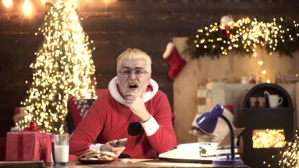 Lustige moderne Weihnachtsmänner halten die Fernbedienung zu Hause. Haus für den Weihnachtsmann. — Stockvideo