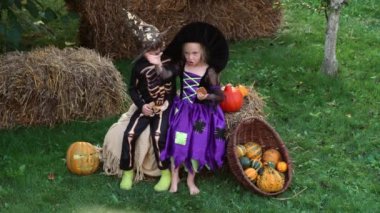 Cadılar Bayramı şapkalı siyah ve turuncu cadı kostümleri giyen çocuklar sonbahar parkında balkabağıyla oynuyorlar. Çocuklar şeker mi şaka mı? Erkek ve kız balkabağı oyuyor..