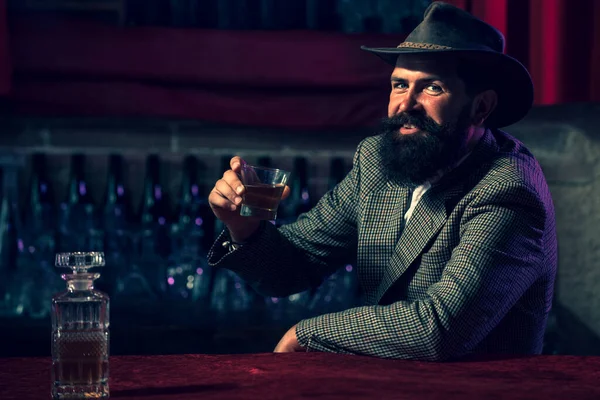 Человек с бородой и усами держит алкогольный напиток на заднем плане бара. Концепция обслуживания и алкоголизма. — стоковое фото
