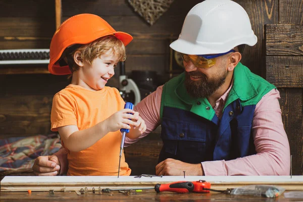 Z 'n zoontje helpt z' n vader met bouwen. Ouder in beschermende helm leren kleine zoon om verschillende gereedschappen te gebruiken in de school workshop. — Stockfoto