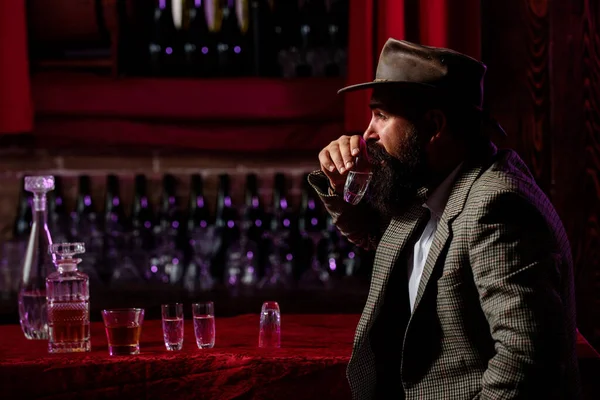 Trabajador vintage con barba larga sosteniendo whisky. Sentado en el bar. — Foto de Stock