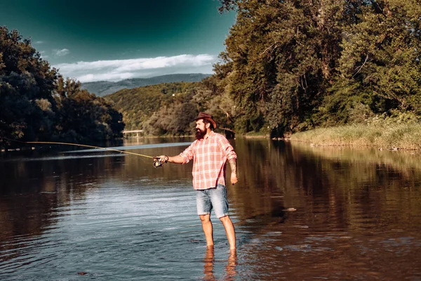 Young bearded man fishing. Man fly fishing. Weekend time. Happy fisherman. In river or on the lake. Fishing skills. Relaxing while enjoying hobby.