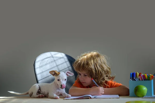 Child with her pet puppy friend. Children and pet education concept - pupil writing to notebook at home.