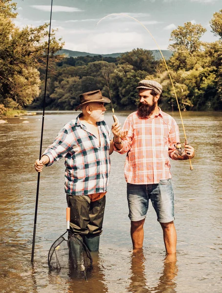 Visser vissen in een rivier met een hengel. Vrolijke grootvader en kleinzoon met hengels op de ligplaats. Vliegvissen in de ongerepte wildernis van Canada. — Stockfoto