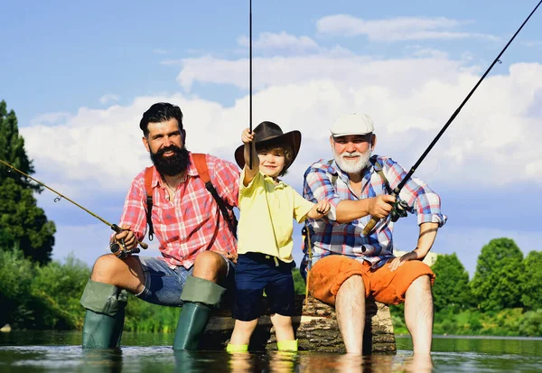 Piccolo ragazzo pesca a mosca su un lago con il padre e il nonno. Giornata estiva. Buon nonno, padre e nipote con canne da pesca sul fiume. Persone felici famiglia hanno pesca e divertimento insieme. — Foto Stock