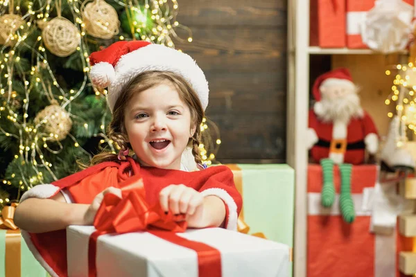 Neujahrskinder. Fröhlich süßes Kind öffnet ein Weihnachtsgeschenk. Weihnachtskind mit roter Geschenkschachtel. Weihnachtsfeier. — Stockfoto