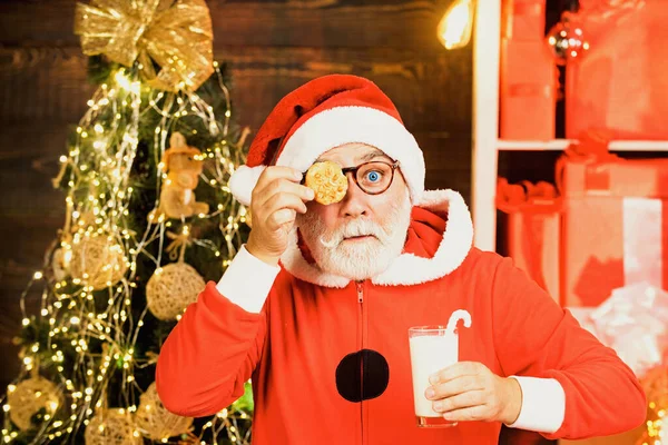 Santa Claus enjoying in served gingerbread cake and milk. Portrait of surprised and funny Santa. Christmas cookies and milk. Christmas for Santa Claus. Greeting Christmas card. — Stock Photo, Image