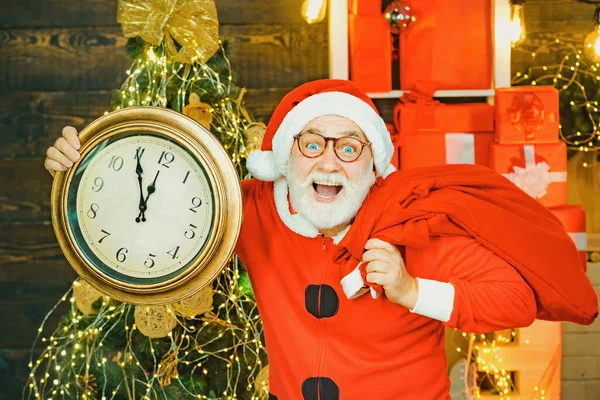 Fünf Minuten bis Silvester oder Weihnachten Mitternacht. Weihnachtsmann. Fröhlich Weihnachtsmann hält Wecker auf Kamin und Weihnachtsbaum Hintergrund. — Stockfoto