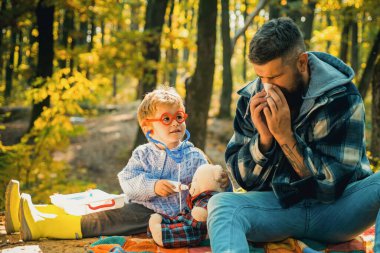 Steteskoplu gözlüklü doktor çocuk hastayı muayene ediyor. Doktor üniformalı çocuk hastayı tedavi ediyor. Eğitim ve geliştirme. Çocuk, babası doğa kökenli doktorculuk oynuyor. Temiz havada oyunlar