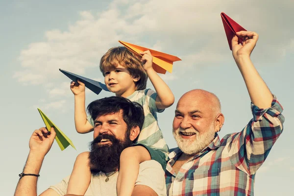 Glückliches Kind, das draußen spielt. Glückliche Männer Familie haben Spaß zusammen. Kinder spielen an sonnigen Tagen mit einfachen Papierfliegern. Vater gibt Sohn Fahrt auf dem Rücken auf blauem Himmel Hintergrund. — Stockfoto