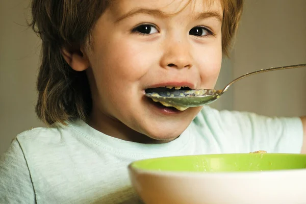 Het kind in de keuken aan tafel aan het eten. Een kind dat eet. Gelukkig kind heeft een ontbijt. Eten en drinken voor kind. Lachen schattig kind baby jongen zitten in de kinderstoel en eten op wazig achtergrond — Stockfoto