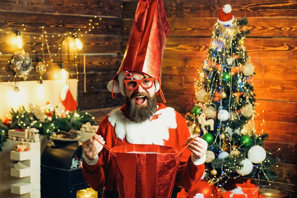 Evde alışveriş çantasıyla çılgın hippi Noel Baba. Noel hazırlığı. Yeni yılı kutlayan adam. Sakallı, modern Noel Baba örgü süveter içinde.. — Stok fotoğraf