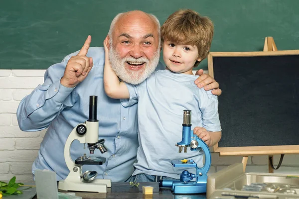 在黑板桌旁的教室里，一位友善的老师。儿童实验显微镜和生物科学。学校教室黑板旁边的老教师。知识日。生物学示范. — 图库照片