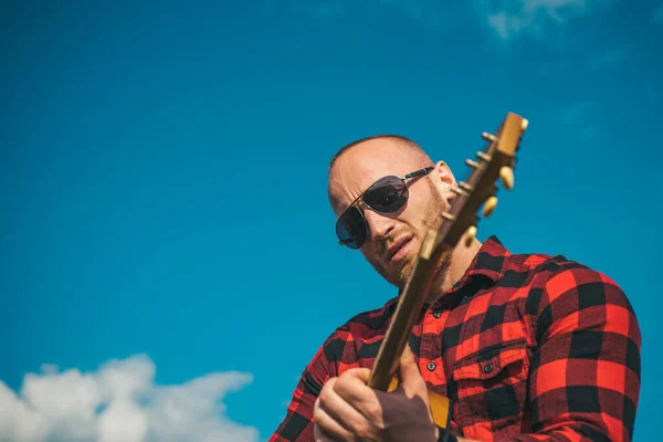 Young man wearing sunglasses and playing guitar on sky. — Stock Photo, Image